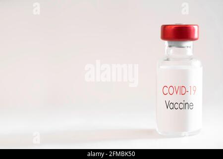 Vaccine bottle with red cap and the English text 'Covid-19 Vaccine' on a white background with shadow. Liquid for injection. Shallow depth of field Stock Photo