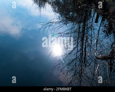 The sun in the blue sky is reflected in the water. Lakes and rivers. Water surface. Sun on a blue sky with clouds. Reflection. Natural landscape. Back Stock Photo