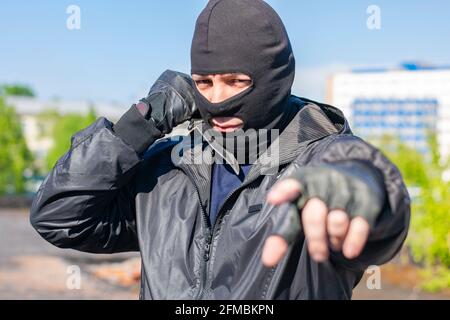 a black masked bandit with a knife in his hand stands in a fighting stance ready to attack and stares into the eyes of the victim Stock Photo