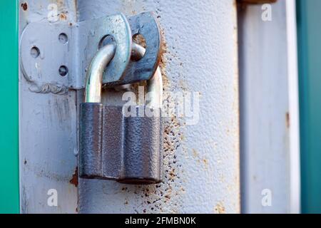Closed padlock hanging on the hinges on the gray iron door Stock Photo