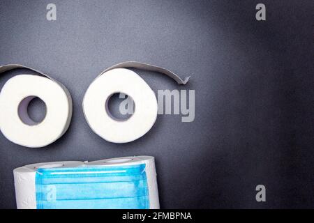 smiley from a medical mask and rolls of toilet paper on a black background. coronavirus panic concept Stock Photo
