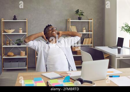 Happy smiling african american businessman with hands behind head sit at desk Stock Photo
