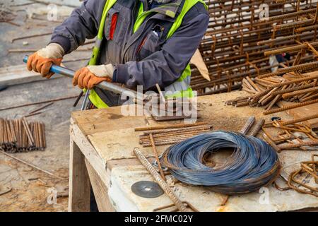 Construction worker bending rebar using manual bending machine at a construction site. Reinforcing metal rods for concrete work. Stock Photo