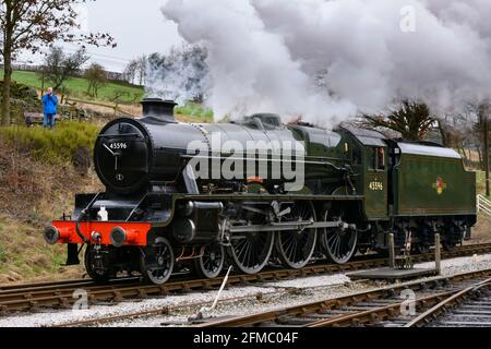 Historic steam train (loco) stationary on track, puffing smoke clouds on scenic rural heritage railway (person & camera) - KWVR, Yorkshire England UK Stock Photo