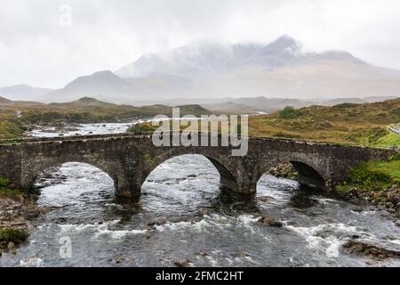 Old three-arched stone bridge over the River Sligachan in the Isle of Skye in Scotland. View on a foggy day Stock Photo