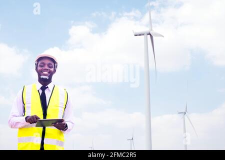 Successful african engineer windmills standing and hoding tablet with wind turbine in background Stock Photo