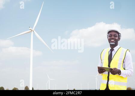 Successful african engineer windmills standing and hoding tablet with wind turbine in background Stock Photo