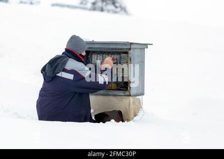 Technician working in the snow and repair telephone line, wiring telephone connection box. Stock Photo
