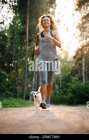 A young slender girl is engaged in fitness in the park with a dog. Stock Photo