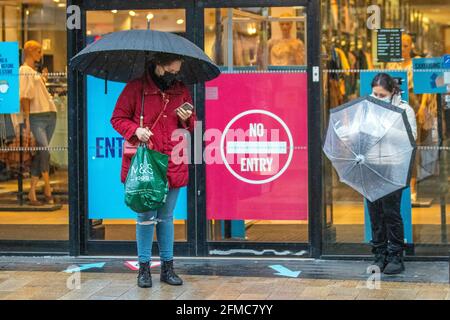 Waiting outside Next in  Preston, Lancashire, UK. 8th May 2021. UK Weather; Wet and windy day in the City Centre. Southerly winds are expected to  bring milder temperatures later in the day.  Credit MediaWorldImages/AlamyLiveNews Stock Photo