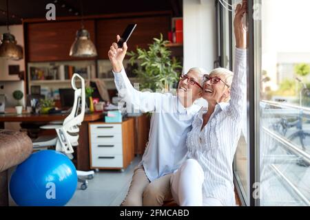 Cheerful senior female colleagues taking a selfie in pleasant atmosphere at workplace. Business, office, job Stock Photo