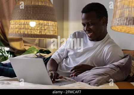 Young positive smiling african man typing on laptop at home Stock Photo