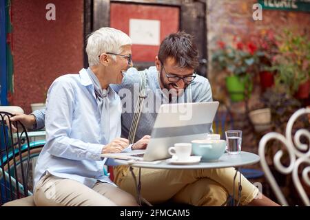 An elderly woman and her young male friend have a good time while having a coffee at bar's garden together on a beautiful day. Leisure, bar, friendshi Stock Photo