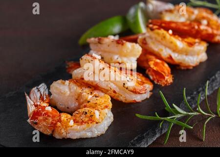 Fried prawn tails with lime and rosemary on black slate platter Stock Photo