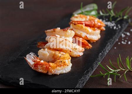 Roasted prawn tails on black slate board with rosemary Stock Photo