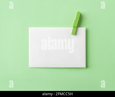 White blank paper with green wooden clothespin on pastel green paper background. Minimalist design template for living green message and greeting card Stock Photo
