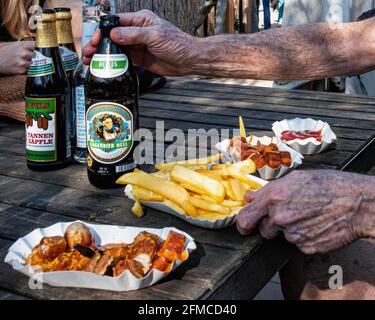 A fast food snack of currywurst and chips at a beer garden at Mauer Park, Prenzlauer Berg, Berlin. Hands of elderly man Stock Photo