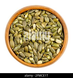 Hulled, roasted, salted pumpkin seeds, in a wooden bowl. Edible, flat, green squash seeds, also known as pepitas, used as a snack. Stock Photo