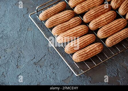 French pastry dessert eclair. Freshly baked aromatic custard cakes cool on the wire rack. Soft selective focus. Stock Photo