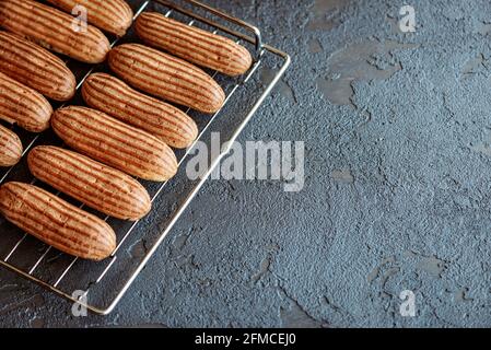French pastry dessert eclair. Freshly baked aromatic custard cakes cool on the wire rack. Soft selective focus. Stock Photo