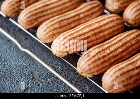 French pastry dessert eclair. Freshly baked aromatic custard cakes cool on the wire rack. Soft selective focus. Stock Photo