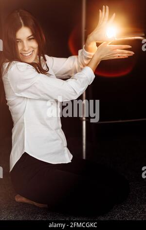 Indoor shot of a sitting charming charismatic and delighted working woman in stylish outfit playing with the light and having fun after a long online Stock Photo