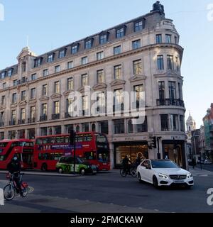 London, Greater London, England - May 04 2021: Traffic and cyclists in Regent Street as the evening light shines on the buildings. Cyclist wears a mas Stock Photo
