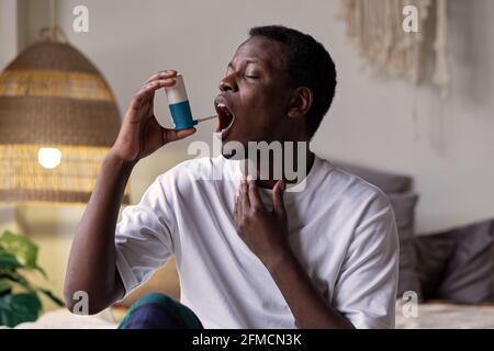 Young african man using asthma inhaler sitting at home Stock Photo