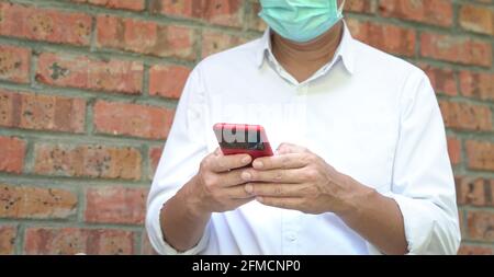 Businessman in face mask standing and using his cellphone for messaging. Focus on fingers and phone. Stock Photo