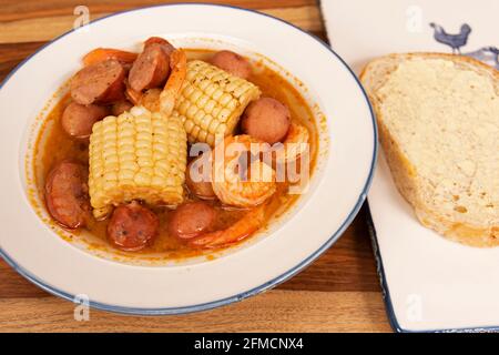 Homemade Cajun Shrimp Boil with corn, new potatoes, and andouille sausage with a slice of sourdough bread, served in a white bowl Stock Photo