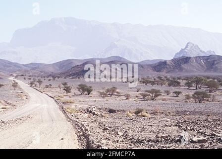 Dirt road through desert in Oman near Al Ayn with mountains in background Stock Photo
