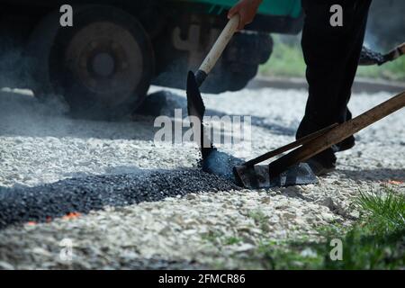 Workers spreading and leveling hot asphalt with tools during road construction Stock Photo