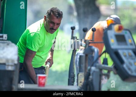 Mihaltsi, Bulgaria - May 7 2021: A road construction worker using a shovel to level asphalt Stock Photo