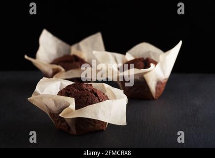 Three homemade chocolate muffins on black background. Stock Photo