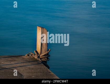 A long exposure photograph of a rope tied to a wooden pier in Swanage, Dorset Stock Photo