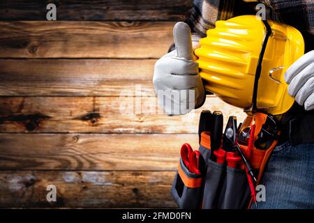 Electrician worker on vintage wooden background; wearing protective gloves and makes OK sign with his thumb up. Construction industry, electrical syst Stock Photo