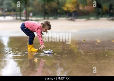 little girl playing with paper boats in puddle Stock Photo