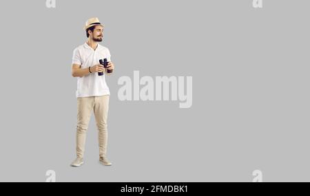 Young man in casual outfit holding binoculars standing on grey copy space background Stock Photo