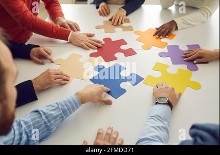 Multiracial businessmen sitting in a circle at a table making up pieces of a colored puzzle. Stock Photo