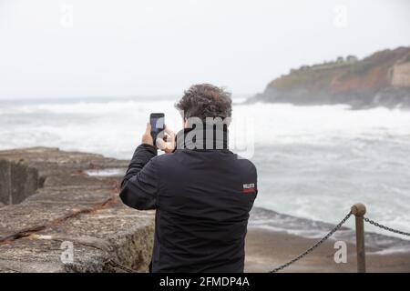 Porthleven,Cornwall,8th May 2021,A man takes a photo of the rough seas  with his phone  in extremely strong winds in Porthleven, Cornwall. The Temperature was 12C and the forecast is for rain & strong winds over the next few days.Credit: Keith Larby/Alamy Live News Stock Photo