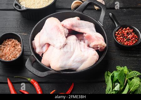 Fresh raw chicken wings with spices and herbs set, in frying cast iron pan, on black wooden table Stock Photo
