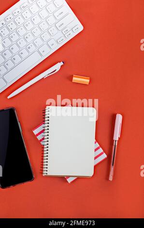 Empty notebook paper, pencil, keyboard, phone and stationery on red background. Back to school, office flat lay. Stock Photo