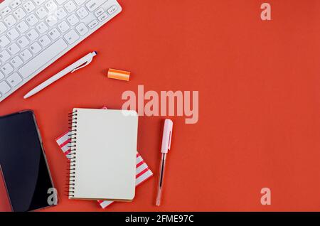 Empty notebook paper, pencil, keyboard, phone and stationery on red background. Back to school, office flat lay. Stock Photo