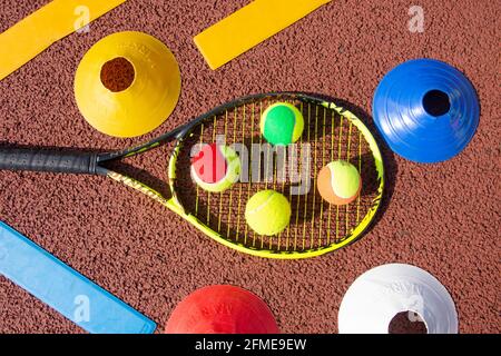 Selection of red, green, orange and yellow tennis balls on tennis racket with lay-downs and cones, Surrey, England, United Kingdom Stock Photo