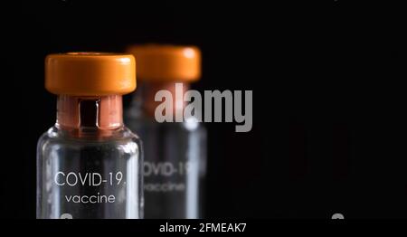 Two corona vaccine vials with orange cap and white English text 'Covid-19 Vaccine' on a black background. Liquid for injection Stock Photo