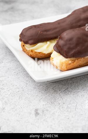 Chocolate eclair with a custard cream filling on a white plate.  With a concrete background Stock Photo