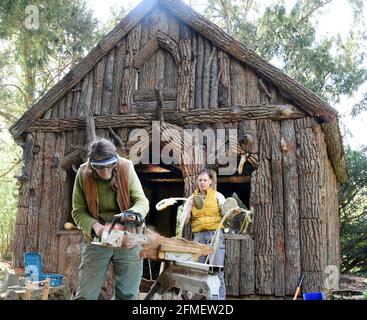 08 May 2021, Saxony-Anhalt, Wörlitz: The graduate restorer Kerstin Klein (r) and the sculptor Katharina Günther apply the last parts of slab boards to missing parts on the over 230-year-old Borkenhäuschen in Wörlitz Park. The small wooden house, also known as Wurzelhütte, has been extensively restored in the last two years. The Borkenhäuschen served Prince Franz as a private bathhouse for changing clothes before swimming in Lake Wörlitz and is clad on the outside with gnarled oak trunks, slabs and bark. Inside, coffers of elm half-trunks and with hand-woven reed mats and rush braids adorn the Stock Photo