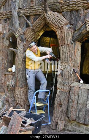 08 May 2021, Saxony-Anhalt, Wörlitz: The graduate restorer Kerstin Klein attaches the last parts of slab boards to missing parts on the over 230-year-old Borkenhäuschen in the Wörlitz Park. The small wooden house, also known as Wurzelhütte, was extensively restored in the last two years. The Borkenhäuschen served Prince Franz as a private bathhouse for changing clothes before swimming in Lake Wörlitz and is clad on the outside with gnarled oak trunks, slabs and bark. Inside, coffers of elm half-trunks and with hand-woven reed mats and rush braids adorn the walls and ceiling. The park was laid Stock Photo