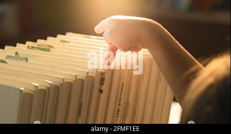 A little cute girl is choosing a book in the bookshelves at home. Stay at home to quarantine from coronavirus pandemic. Homeschool concept. Stock Photo