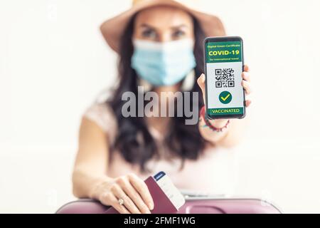 Vaccinated woman shows her digital green certificate for Covid-19 in her mobile phone with passport and flight ticket, face mask on, ready to go. Stock Photo